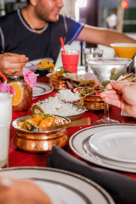 Guests enjoying a lively and exceptional dining experience at Mint Indian Restaurant, sharing a table filled with food and colorful cocktails.