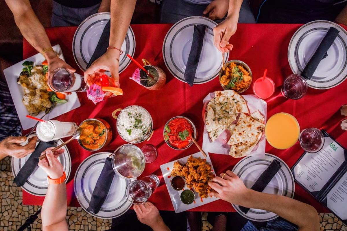 Guests enjoying a lively and exceptional dining experience at Mint Indian Restaurant, sharing a table filled with food and colorful cocktails.
