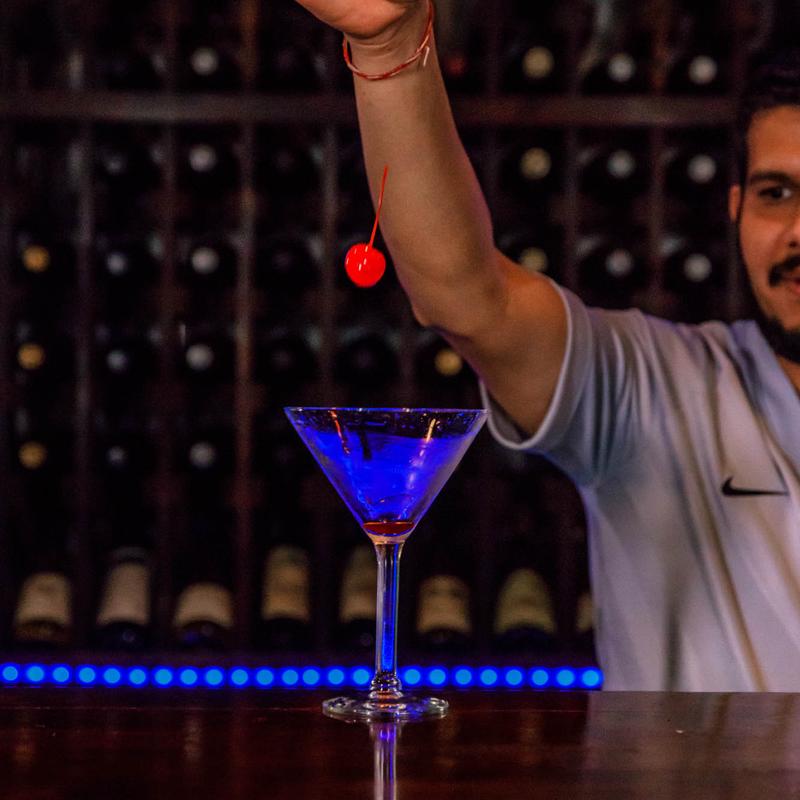 A bartender at Mint Indian Restaurant and Lounge expertly pouring a freshly shaken, handcrafted cocktail into a martini glass.