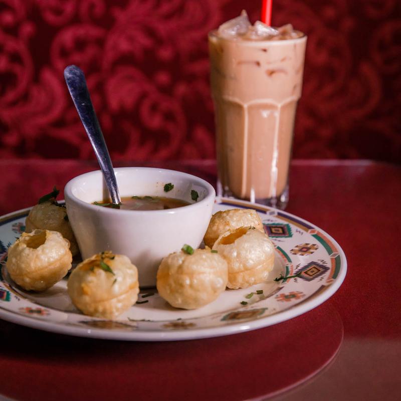 A plate of Pani Puri, a popular Indian street food appetizer from Mint Restaurant, served with savory dipping water and a refreshing iced beverage.