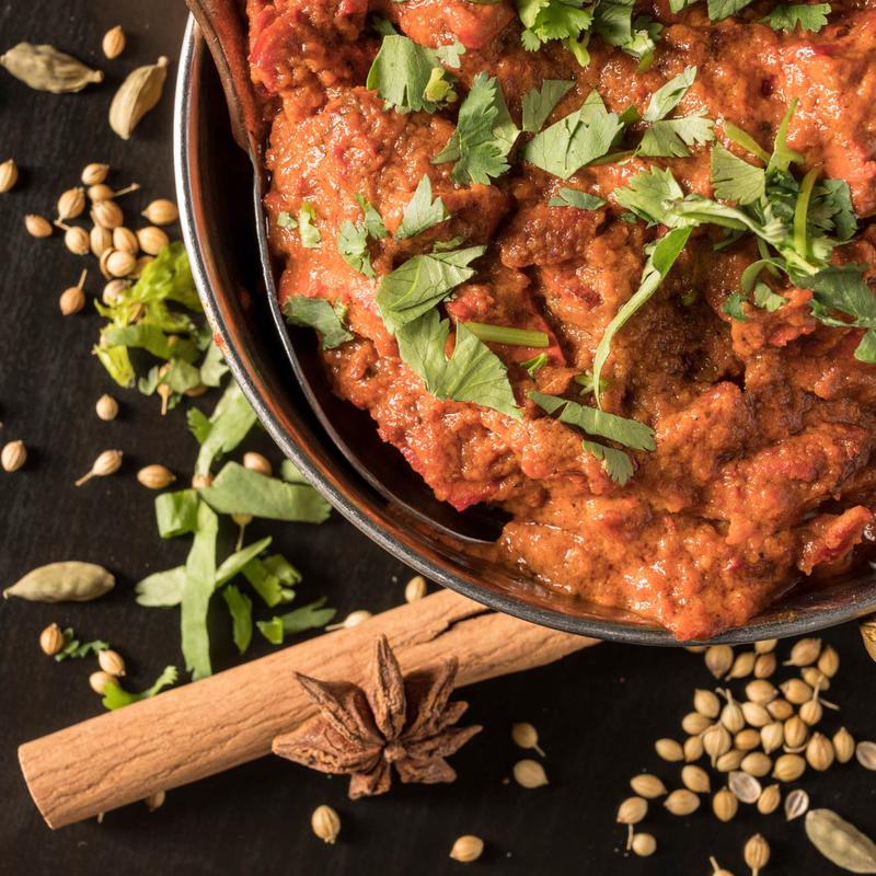 An artfully presented bowl of authentic Butter Chicken from Mint Indian Restaurant, served in a traditional hammered copper karahi and surrounded by whole spices.