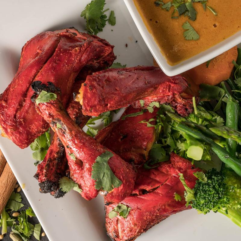 A healthy and delicious plate of grilled Kalmi Kebab, served with fresh steamed vegetables, a lime wedge, and a savory dipping sauce.