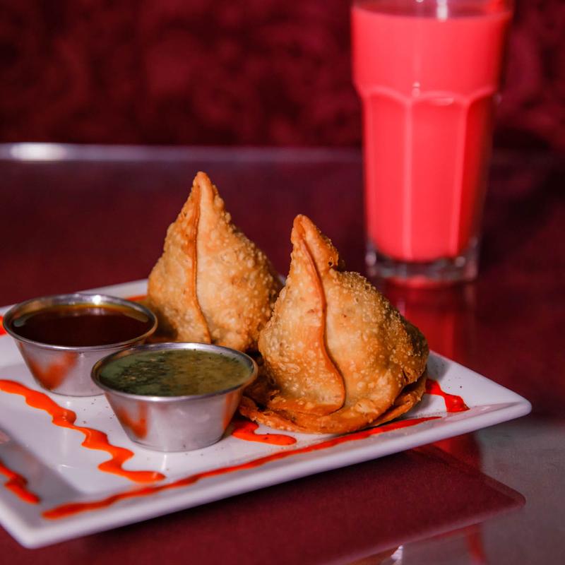 Two perfectly fried vegetable Samosas from Mint Indian Restaurant, served with classic mint and tamarind chutneys on a beautifully presented plate.
