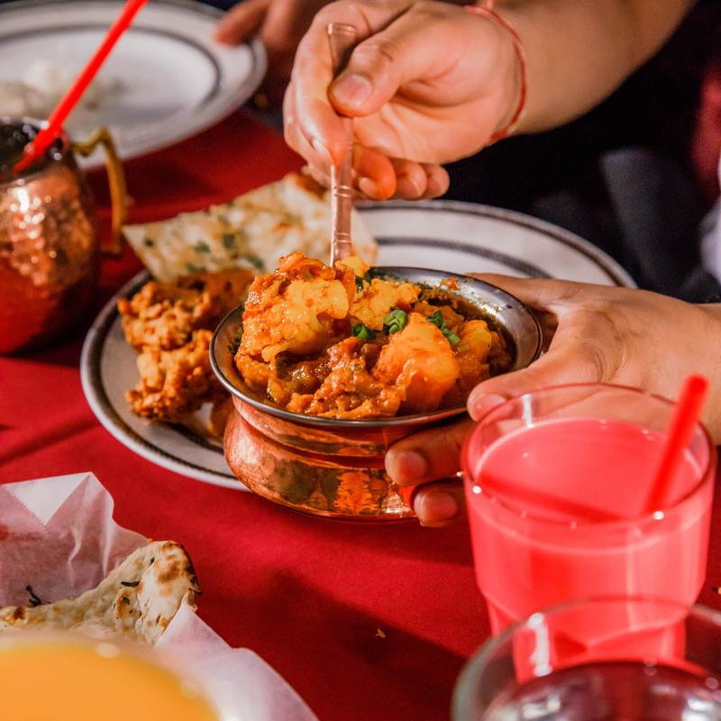 Guests enjoying a lively and exceptional dining experience at Mint Indian Restaurant, sharing a table filled with food and colorful cocktails.