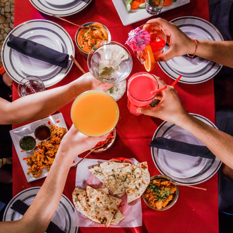 Guests enjoying a lively and exceptional dining experience at Mint Indian Restaurant, sharing a table filled with food and colorful cocktails.