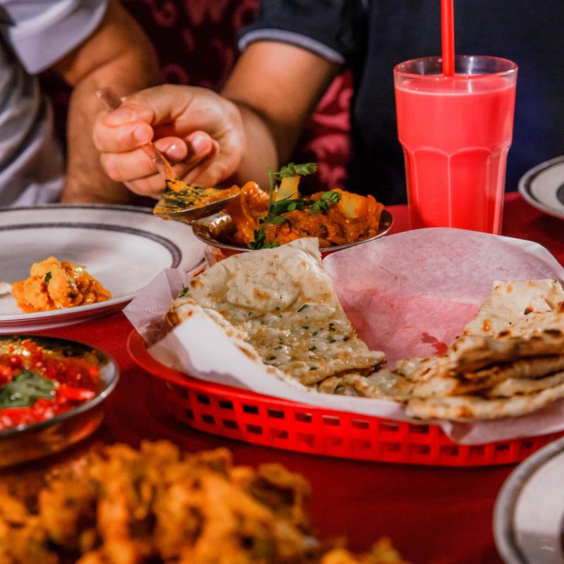 Guests enjoying a lively and exceptional dining experience at Mint Indian Restaurant, sharing a table filled with food and colorful cocktails.