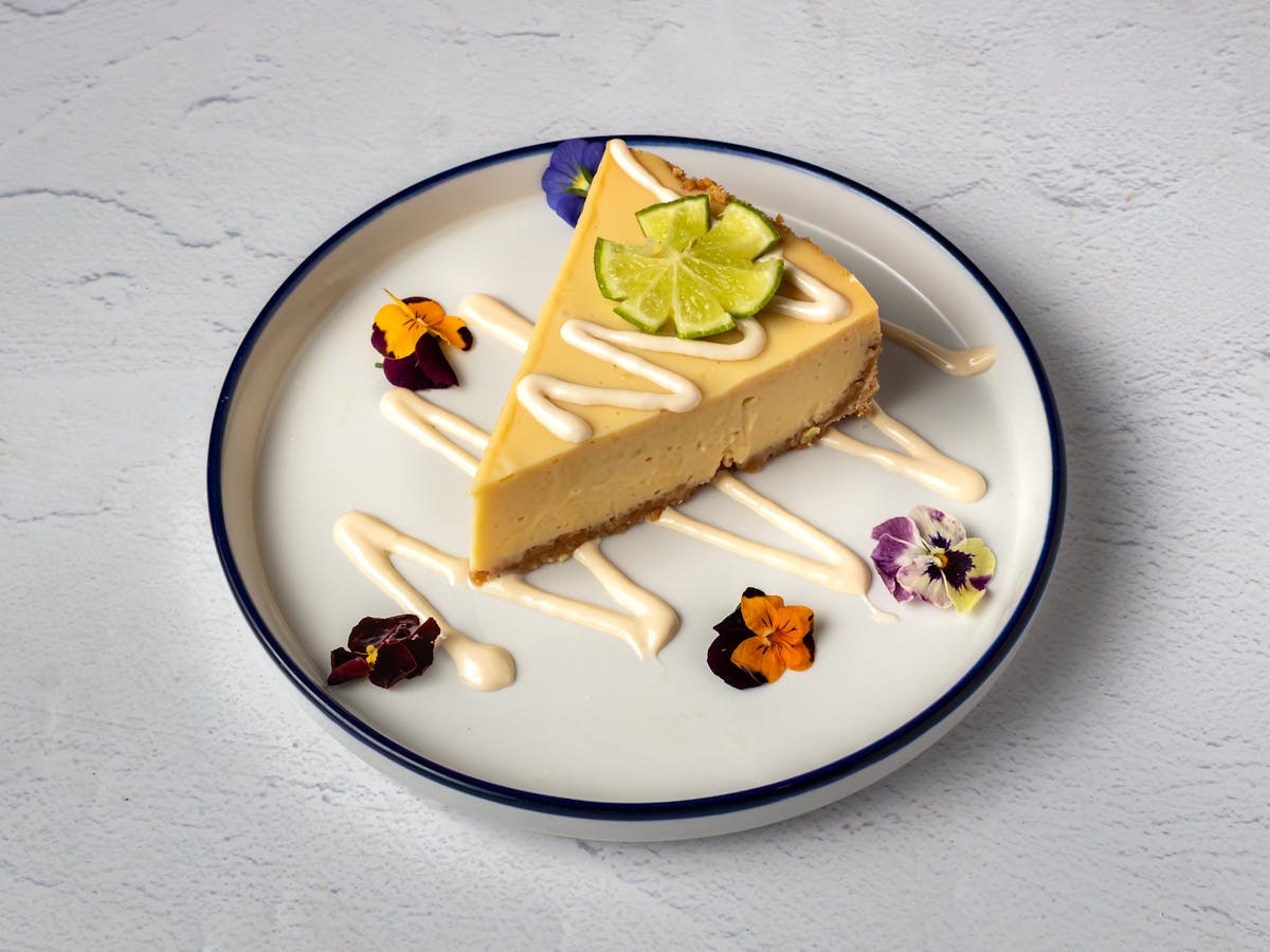 Key Lime Cheesecake with fresh lime, edible flowers, and house-made cream drizzle — Italian dessert at Amici Brick Oven Pizza, West Palm Beach