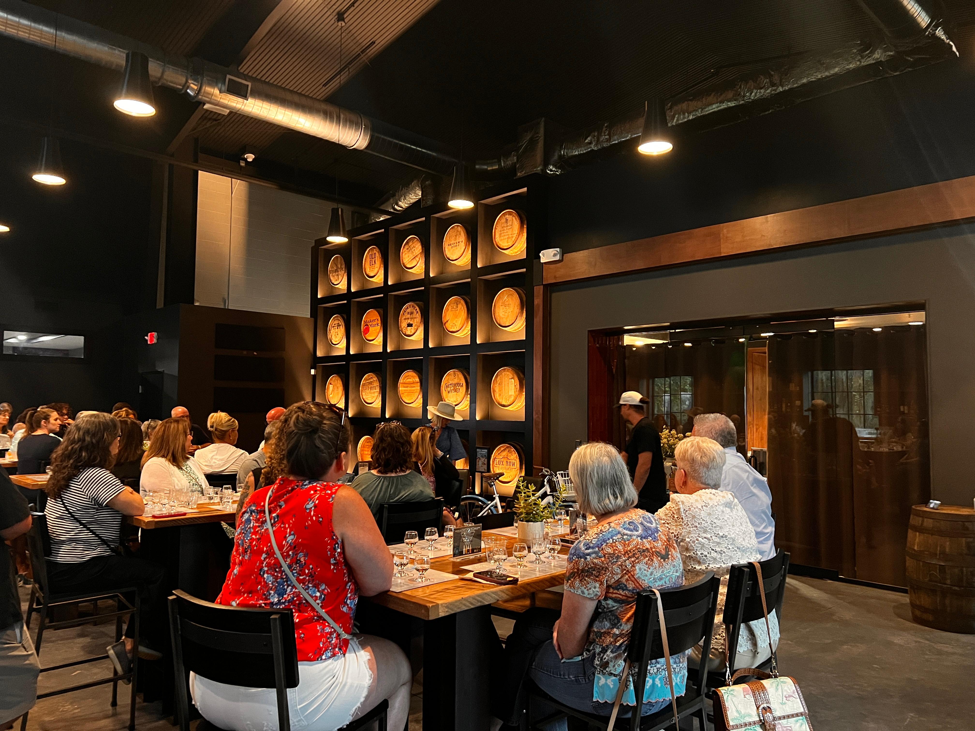 People sitting at a table sampling whiskey for a private tasting with a barrel wall in the background