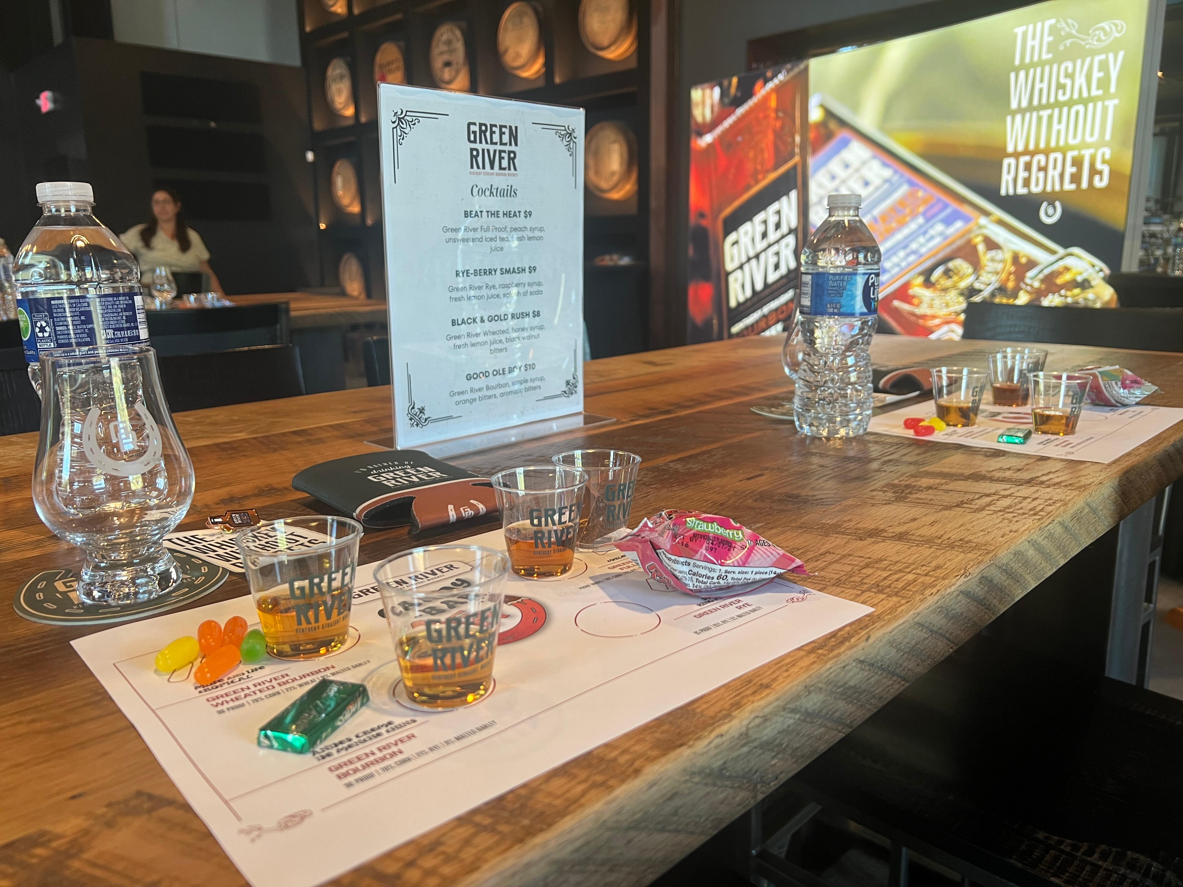 A paper with descriptions of candies and Green River Whiskies with small sample cups of whiskies on a table