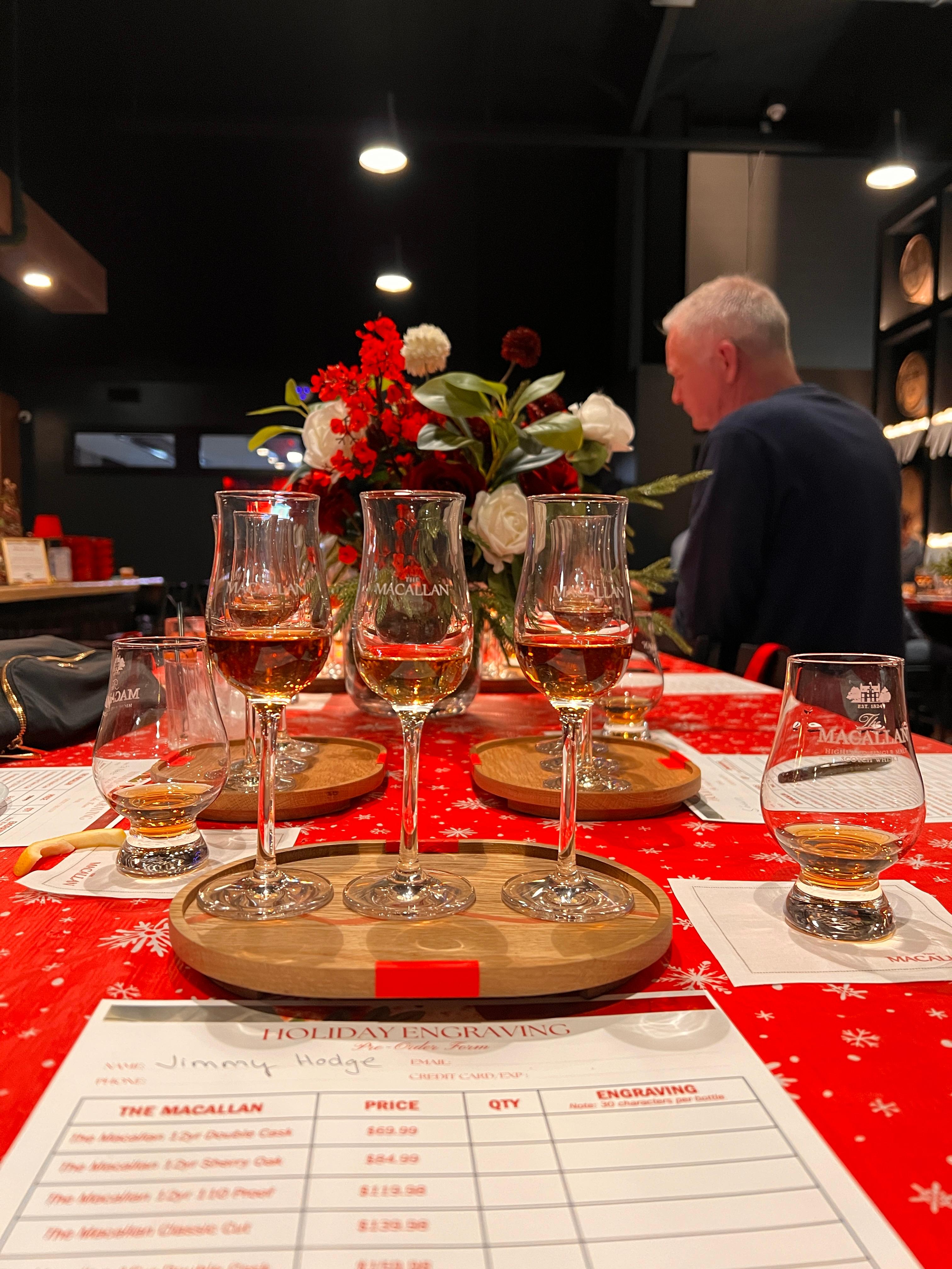Macallan samples poured into Macallan glasses on a nice piece of wood on a table decorated with red table cloth and red mini lamps. Papers with Macallan descriptions.