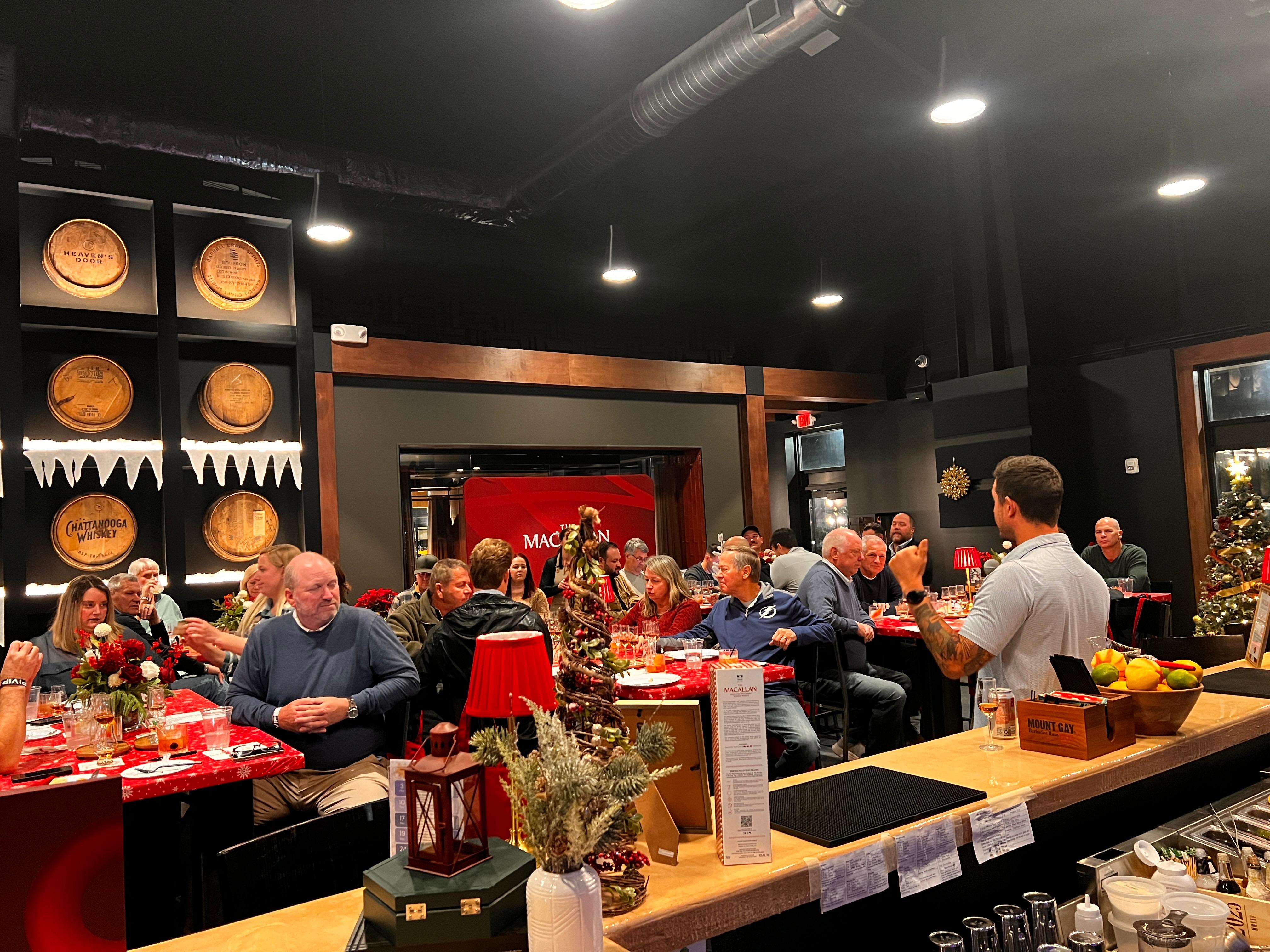 A group of people gathered at multiple tables listening to the Macallan Brand Ambassador speak