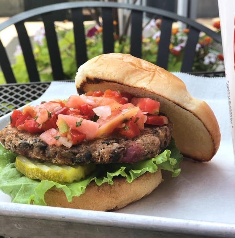 Burger Fresh burger with tomatoes, pickle and lettuce on a tray on a patio table